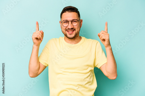 Young hispanic man isolated on blue background indicates with both fore fingers up showing a blank space.