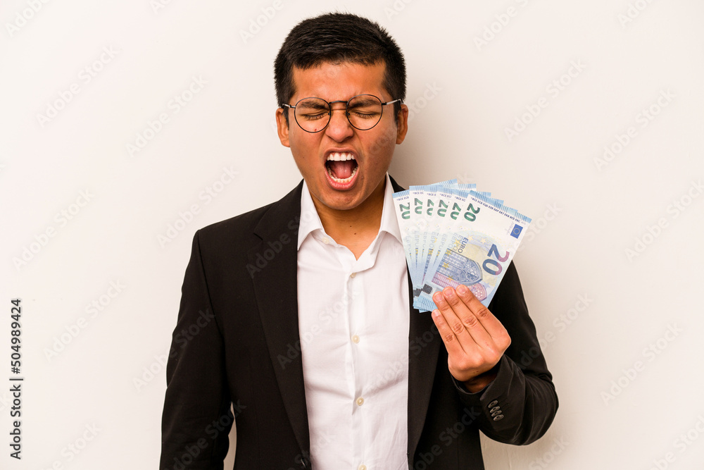 Young hispanic business man holding banknotes isolated on white background screaming very angry and aggressive. Young hispanic business man holding banknotes isolated on white background screaming very angry and aggressive.