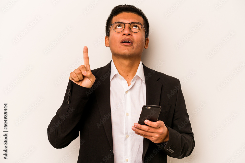 Young business hispanic man holding mobile phone isolated on white background pointing upside with opened mouth. Young business hispanic man holding mobile phone isolated on white background pointing upside with opened mouth.