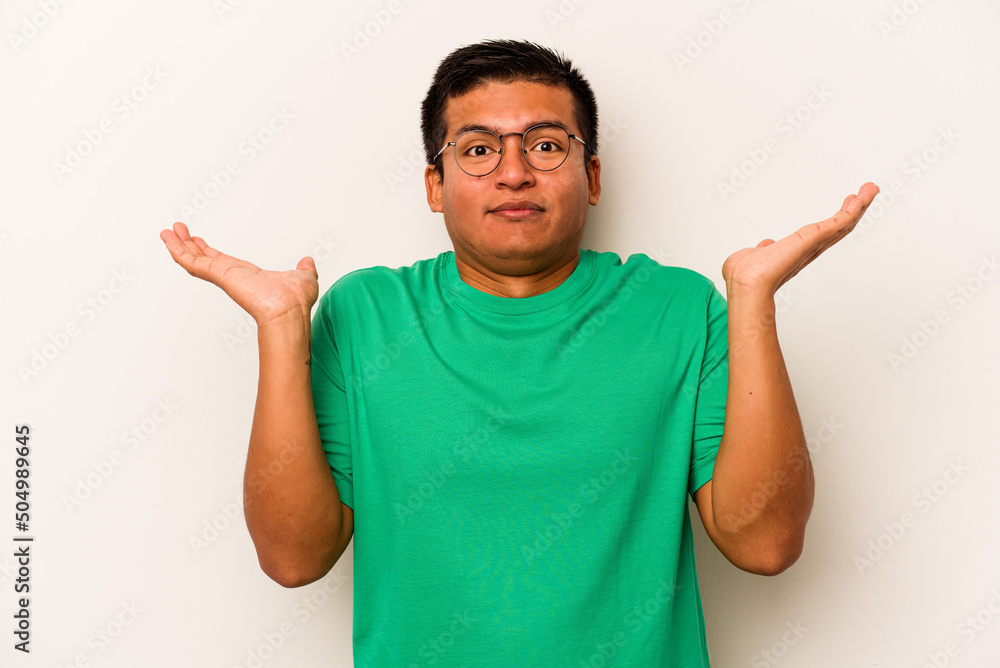 Young hispanic man isolated on white background confused and doubtful shrugging shoulders to hold a copy space. Young hispanic man isolated on white background confused and doubtful shrugging shoulders to hold a copy space.