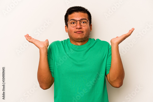 Young hispanic man isolated on white background confused and doubtful shrugging shoulders to hold a copy space.