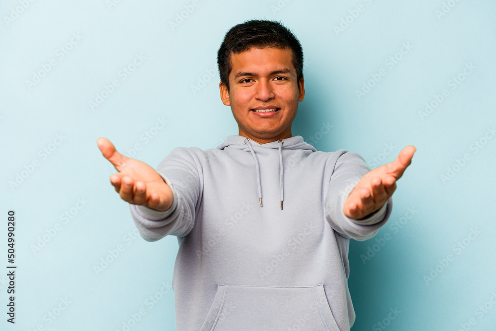 Young hispanic man isolated on blue background showing a welcome expression. Young hispanic man isolated on blue background showing a welcome expression.