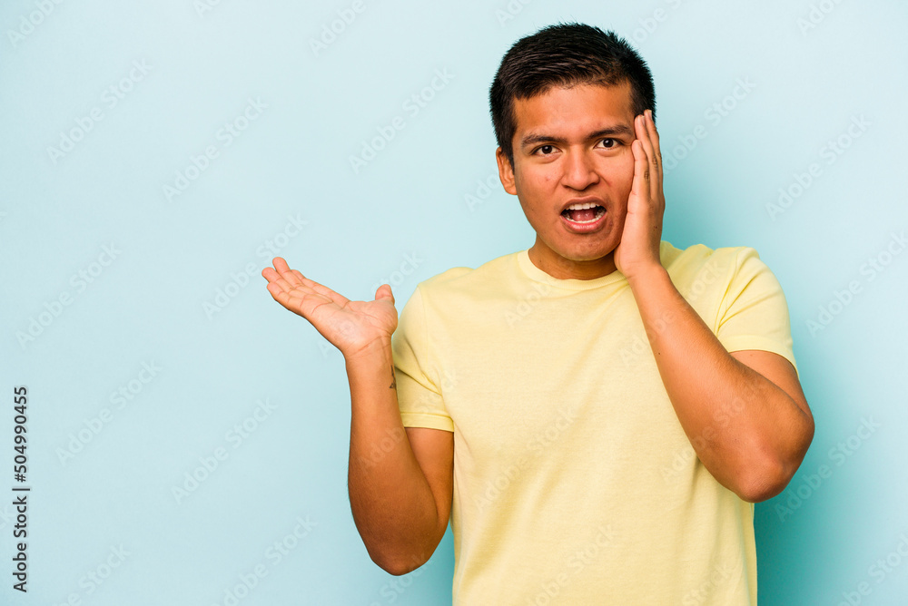 Young hispanic man isolated on blue background impressed holding copy space on palm. Young hispanic man isolated on blue background impressed holding copy space on palm.