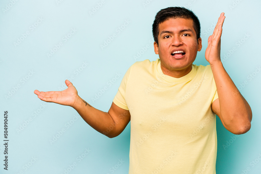 Young hispanic man isolated on blue background holds copy space on a palm, keep hand over cheek. Amazed and delighted. Young hispanic man isolated on blue background holds copy space on a palm, keep hand over cheek. Amazed and delighted.