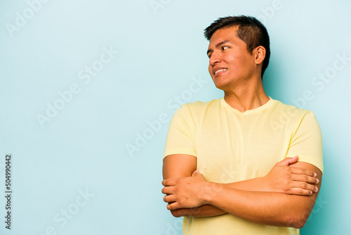 Young hispanic man isolated on blue background smiling confident with crossed arms.