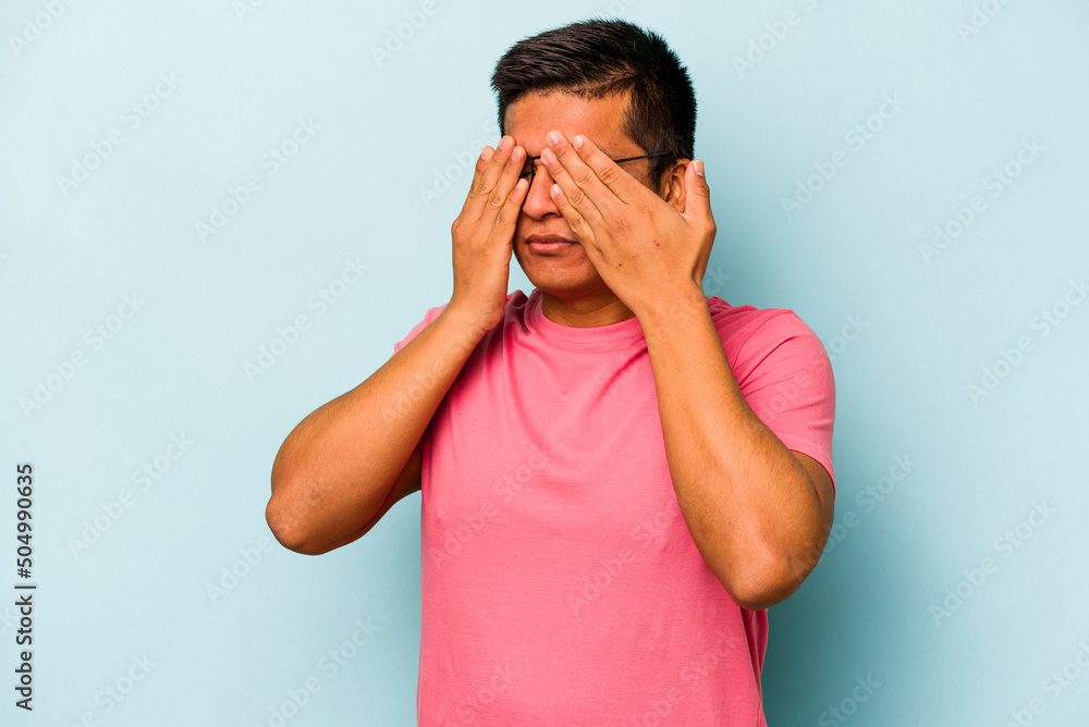 Young hispanic man isolated on blue background afraid covering eyes with hands. Young hispanic man isolated on blue background afraid covering eyes with hands.