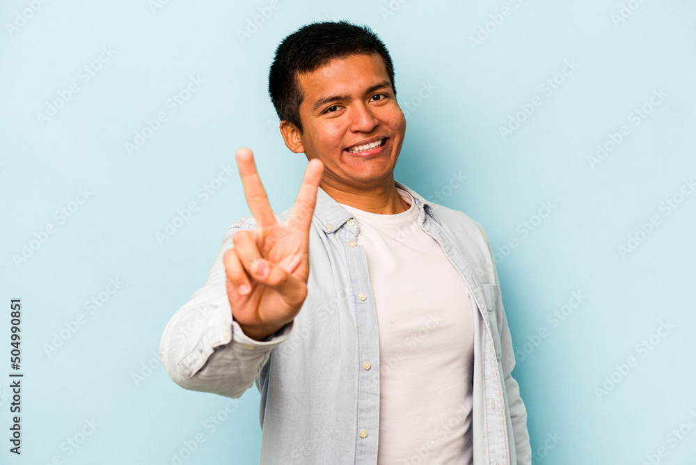 Young hispanic man isolated on blue background joyful and carefree showing a peace symbol with fingers. Young hispanic man isolated on blue background joyful and carefree showing a peace symbol with fingers.