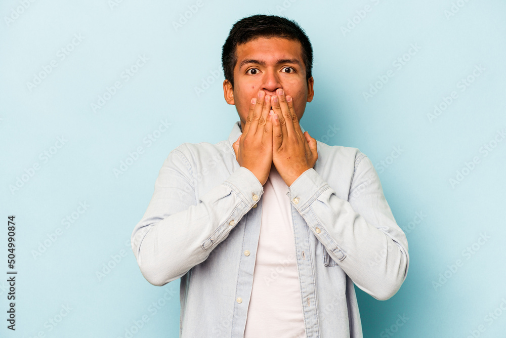 Young hispanic man isolated on blue background covering mouth with hands looking worried. Young hispanic man isolated on blue background covering mouth with hands looking worried.
