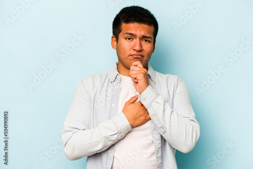 Young hispanic man isolated on blue background thinking and looking up, being reflective, contemplating, having a fantasy.