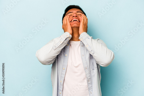 Young hispanic man isolated on blue background laughs joyfully keeping hands on head. Happiness concept.