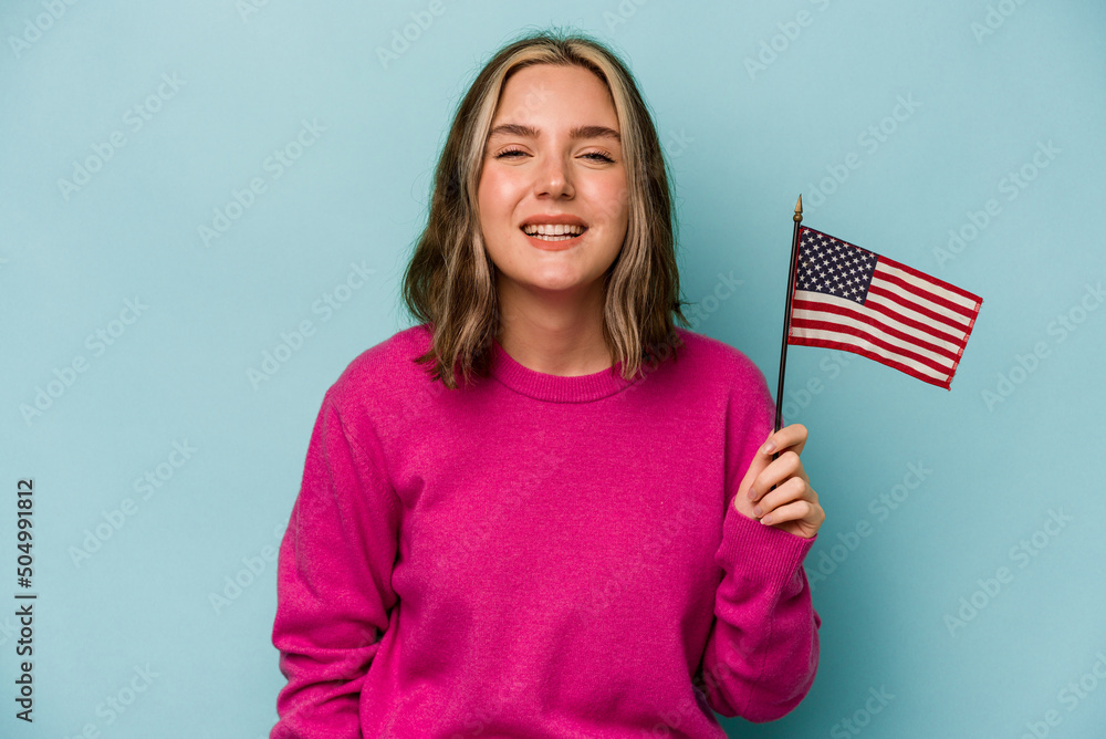 Young caucasian woman holding a American flag isolated on blue background laughing and having fun. Young caucasian woman holding a American flag isolated on blue background laughing and having fun.