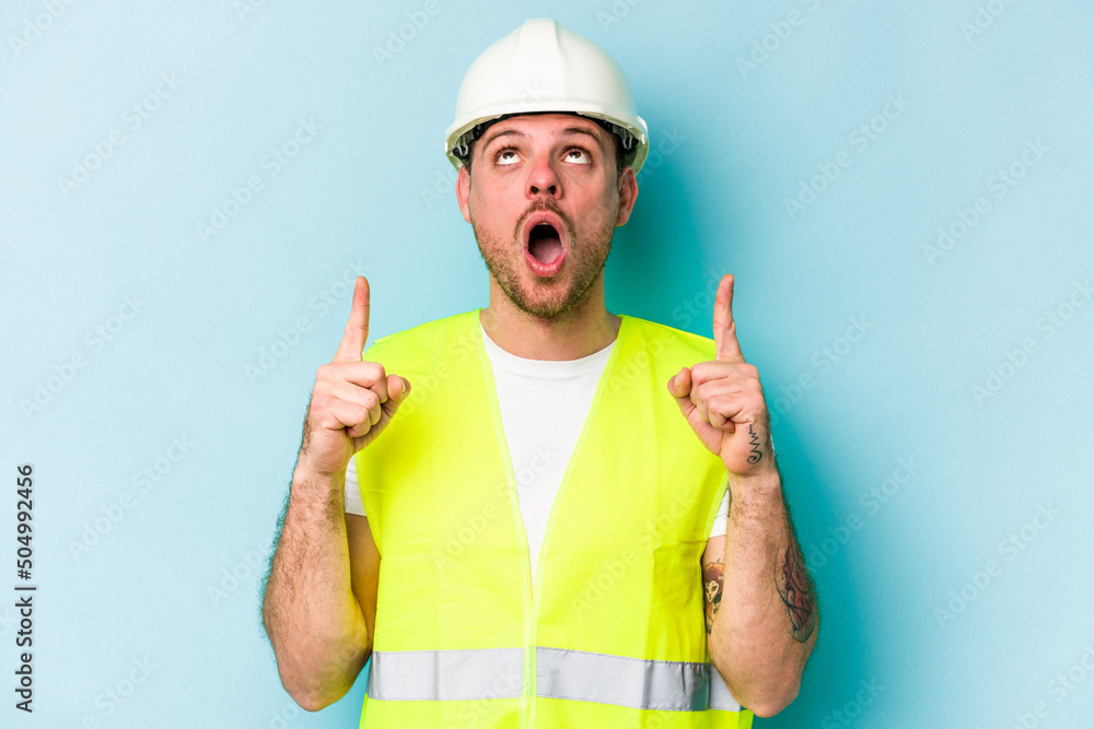 Young laborer caucasian man isolated on blue background pointing upside with opened mouth.