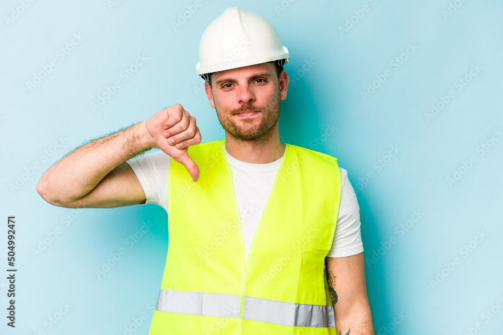 Young laborer caucasian man isolated on blue background showing a dislike gesture, thumbs down. Disagreement concept.