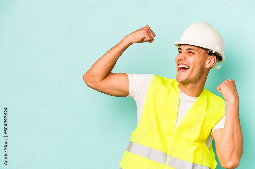 Young laborer caucasian man isolated on blue background raising fist after a victory, winner concept.
