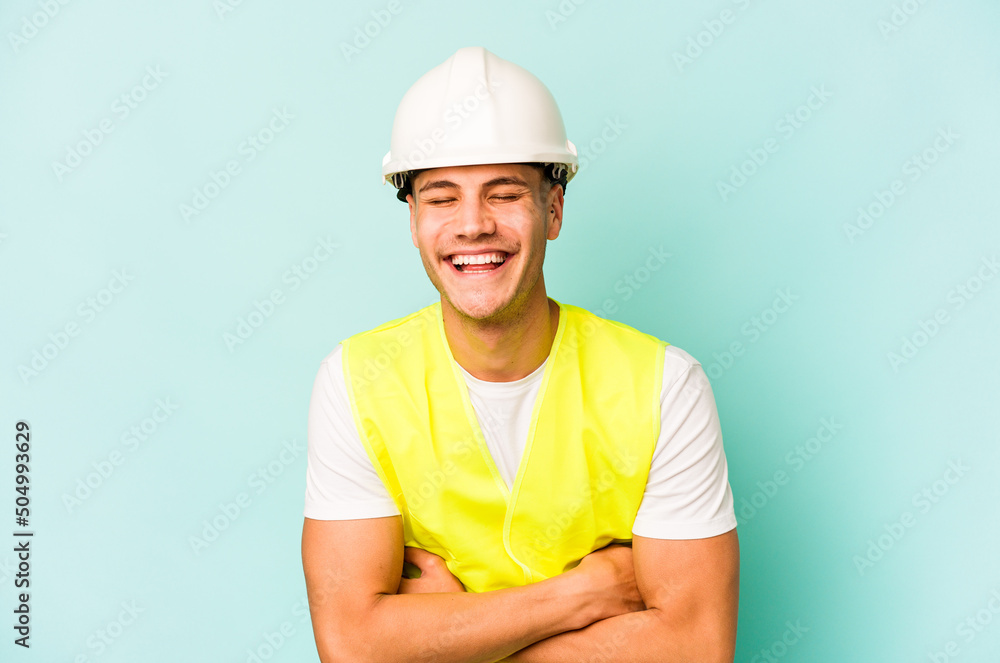 Young laborer caucasian man isolated on blue background laughing and having fun.
