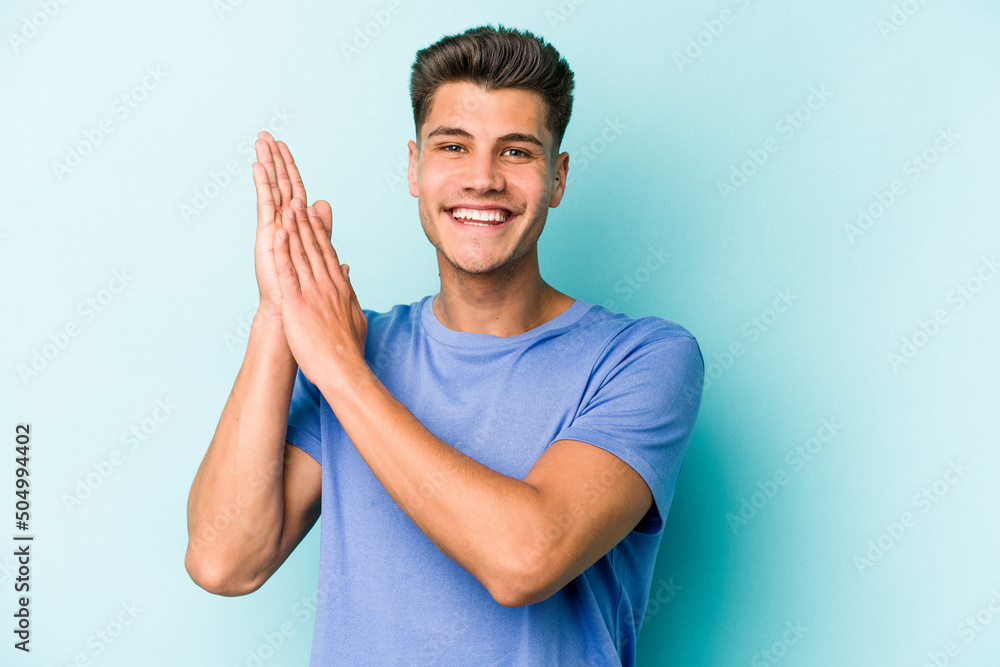 Young caucasian man isolated on blue background feeling energetic and comfortable, rubbing hands confident. Young caucasian man isolated on blue background feeling energetic and comfortable, rubbing hands confident.