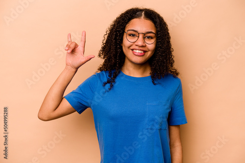 Tela Young African American woman isolated on beige background showing a horns gesture as a revolution concept