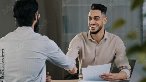 Two successful diverse business men colleague arabian salesman banker male manager shaking hand client customer accept common project successful corporate partnership deal agreement at office meeting