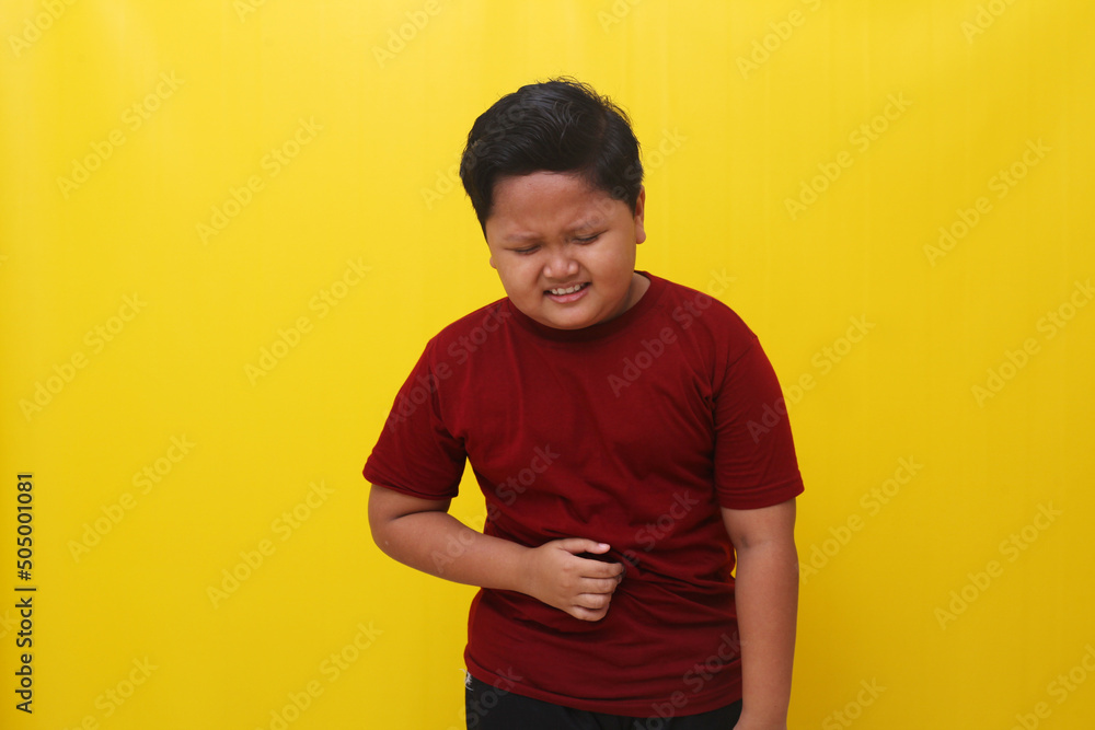 Asian boy having problems with stomach. Isolated on yellow background Asian boy having problems with stomach. Isolated on yellow background