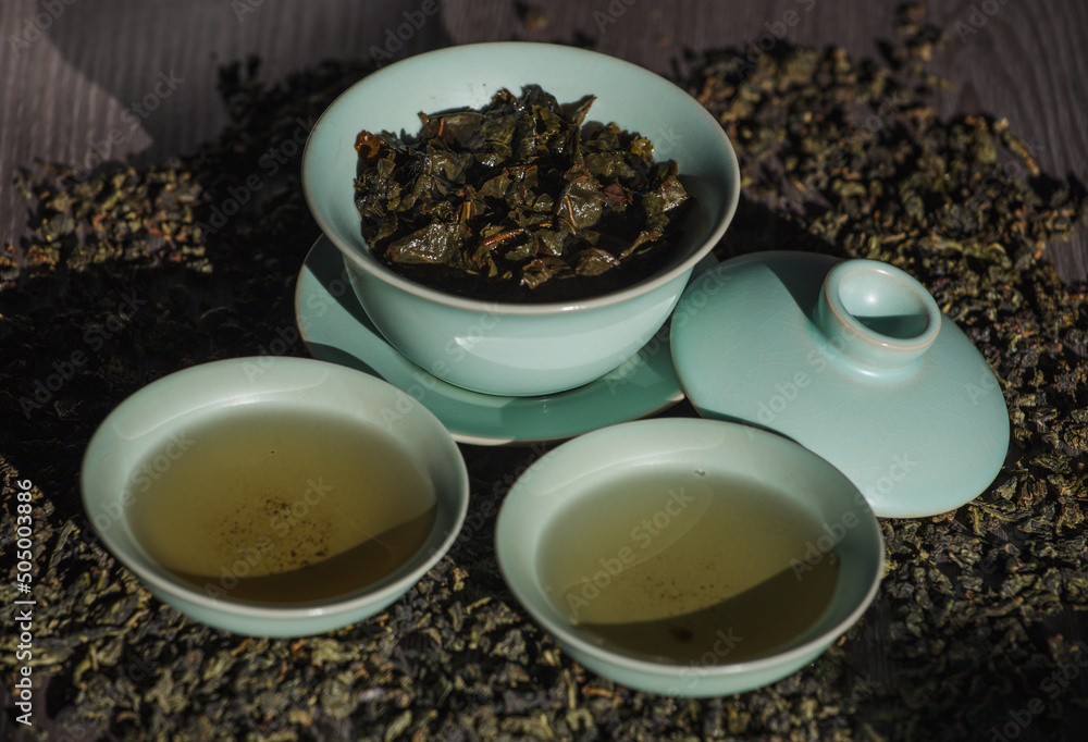 Gaivan and bowls with green tea and tea leaves on a brown background close-up, selective focus. Tea ceremony. Traditional Chinese tea ware. Gaivan and bowls with green tea and tea leaves on a brown background close-up, selective focus. Tea ceremony. Traditional Chinese tea ware.