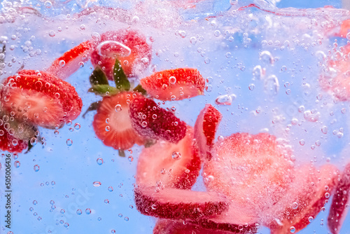 Sliced Strawberry in water with water splash and air bubbles on blue background. Close up image.