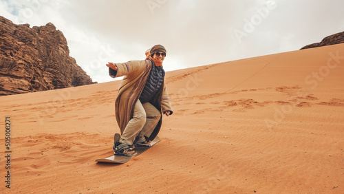 Photography Young woman posing as sand dune surfing wearing bisht - traditional Bedouin coat