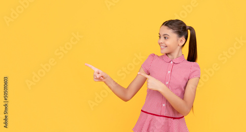 happy kid pointing finger on yellow background copy space, announcement photo