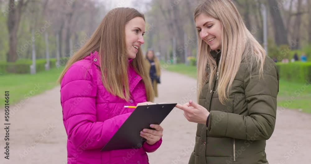 Opinion poll. A woman interviewing people, conducting survey standing outdoor Opinion poll. A woman interviewing people, conducting survey standing outdoor