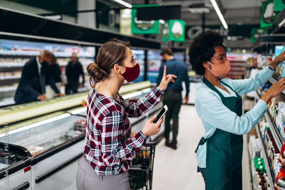 Young woman with face protective mask is buying groceries at the supermarket and talking with emloyee. Covid-19, Coronavirus, newnormal concept. Young woman with face protective mask is buying groceries at the supermarket and talking with emloyee. Covid-19, Coronavirus, newnormal concept.