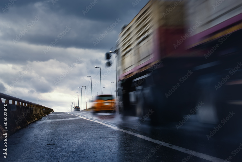 Blurry of lorry truck driving fast on bridge during hard rain fall with storm cloud as background,selective focus.Concept of rainy season,.transportation, busines distribution and logistics
