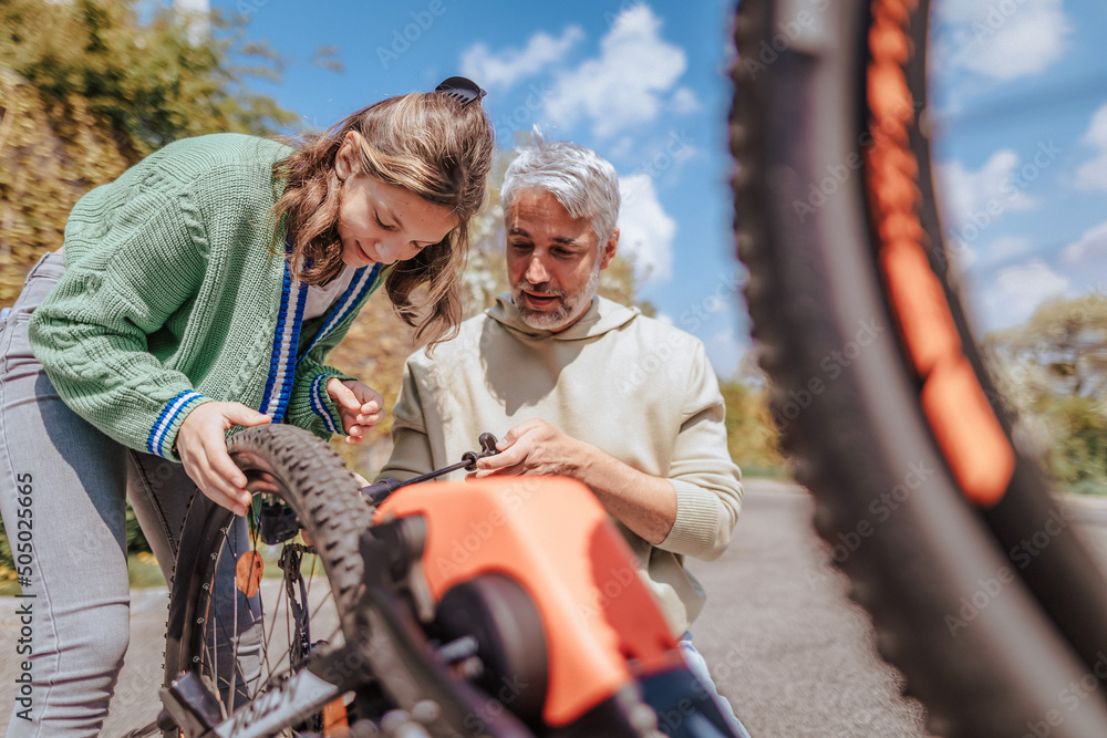 Obraz premium Happy father with teenage daughter repairing bicycle in street in town.