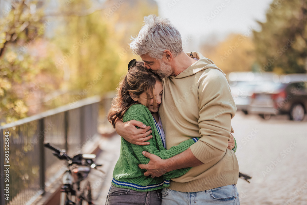 Teenage daughter hugging her father outside in town when spending time together. - obrazy, fototapety, plakaty 