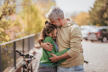 Teenage daughter hugging her father outside in town when spending time together.