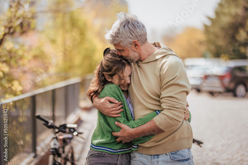 Teenage daughter hugging her father outside in town when spending time together.
