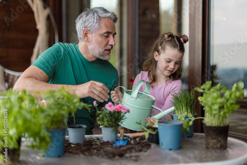 Little daughter helping father to plant and water flowers, home gardening concept
