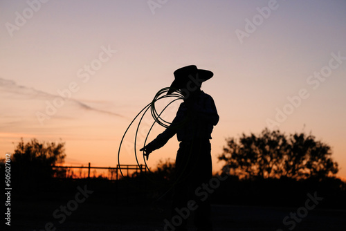 Young cowboy with rope in Texas sunset on ranch for childhood western lifestyle. photo