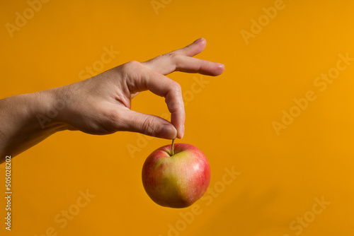 female hand holding a red apple on a yellow background