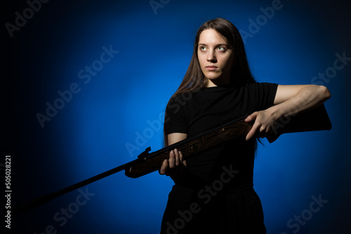 a young girl with long flowing hair in a black T-shirt with a gun in her hands on a dark background