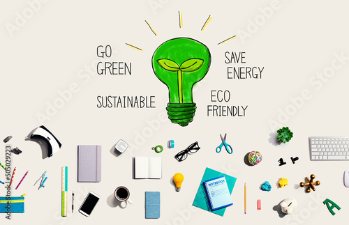 Green light bulb with collection of electronic gadgets and office supplies