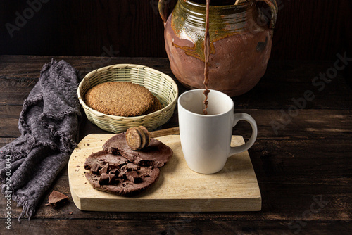 sirviendo taza de chocolate artesanal con champurradas integrales e ingredientes sobre mesa de madera antigua photo