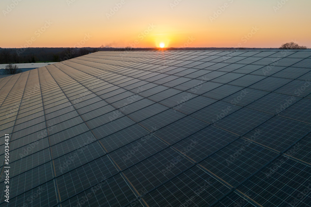Blue photovoltaic solar panels mounted on building roof for producing clean ecological electricity at sunset. Production of renewable energy concept - obrazy, fototapety, plakaty 