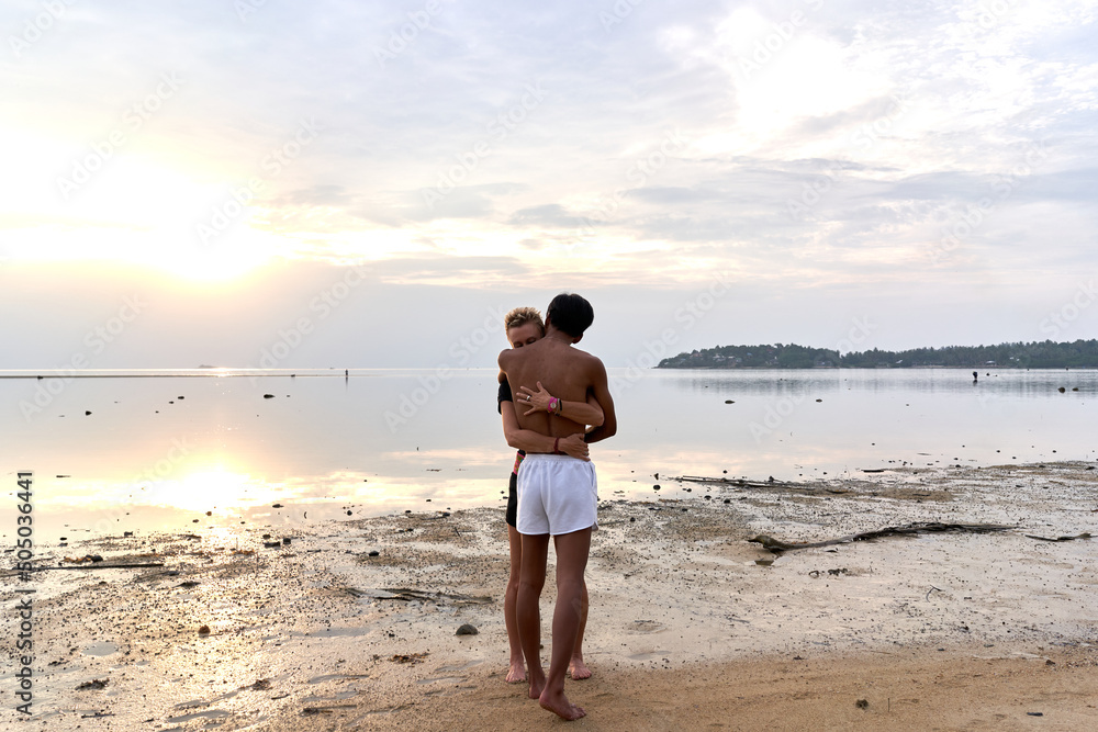 Multicultural couple embracing while standing next to the sea during sunset Multicultural couple embracing while standing next to the sea during sunset