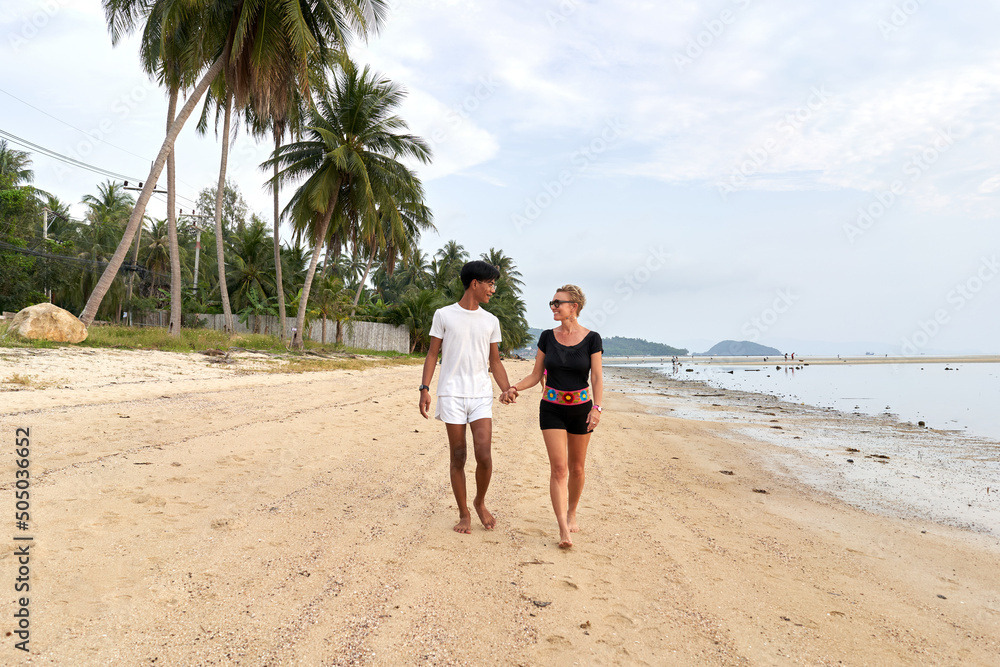 Multiethnic couple walking together in a sandy tropical beach