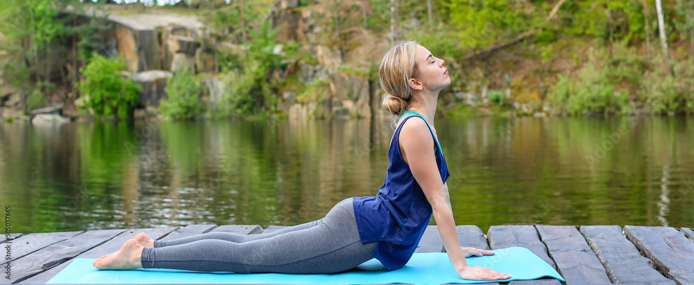 Beautiful young woman practicing yoga near lake - obrazy, fototapety, plakaty 