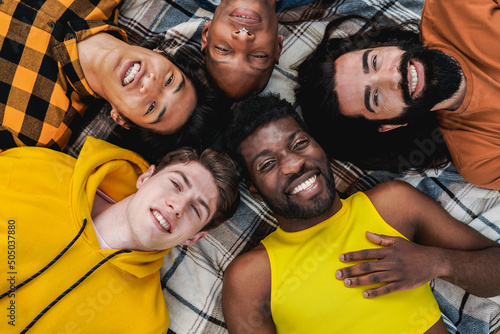 Diverse trendy group of friends having fun together outdoor lying in circle - Diversity and multiethnic people - Focus on gay man with make up on