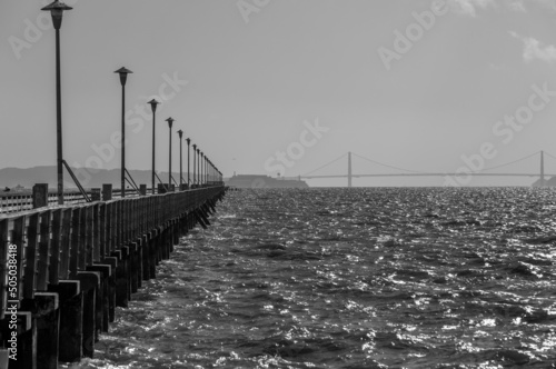 Dramatic black and white image of the Berkeley Marina, with the pier and piers lights fading into the horizon, and Golden Gate Bridge in background.