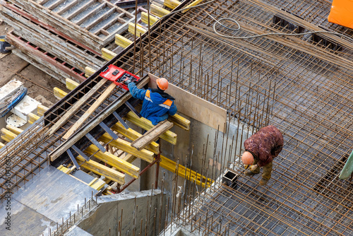 Builders in orange helmets make a steel reinforcement cage for pouring a concrete slab. Steel rods and metal formwork on a construction site. Monolithic construction. Cast-in-place concrete photo