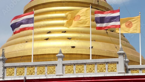 The Thai national flags and The Ddhammacakka flags flutters beside golden pagoda at Buddhist temple photo