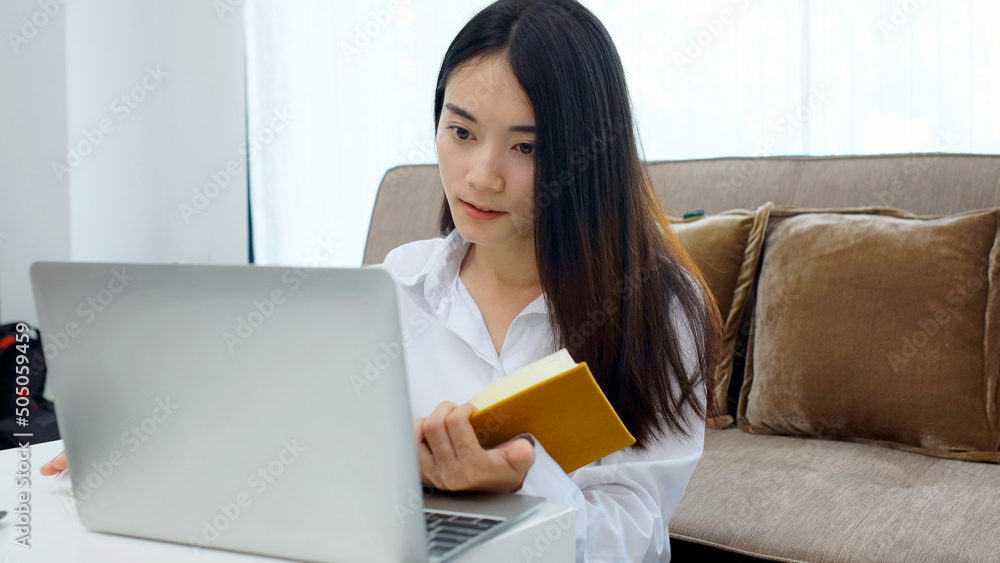 Happy asian women working online with laptop computer at home office, Asia female smiling while writting on noebook paper, online education Happy asian women working online with laptop computer at home office, Asia female smiling while writting on noebook paper, online education