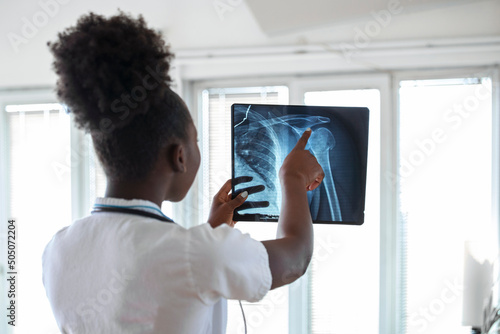 Woman doctor in hospital looking at x-ray film healthcare, roentgen, people and medicine concept. Young smiling female doctor with stethoscope pointing at X-ray at doctor's office